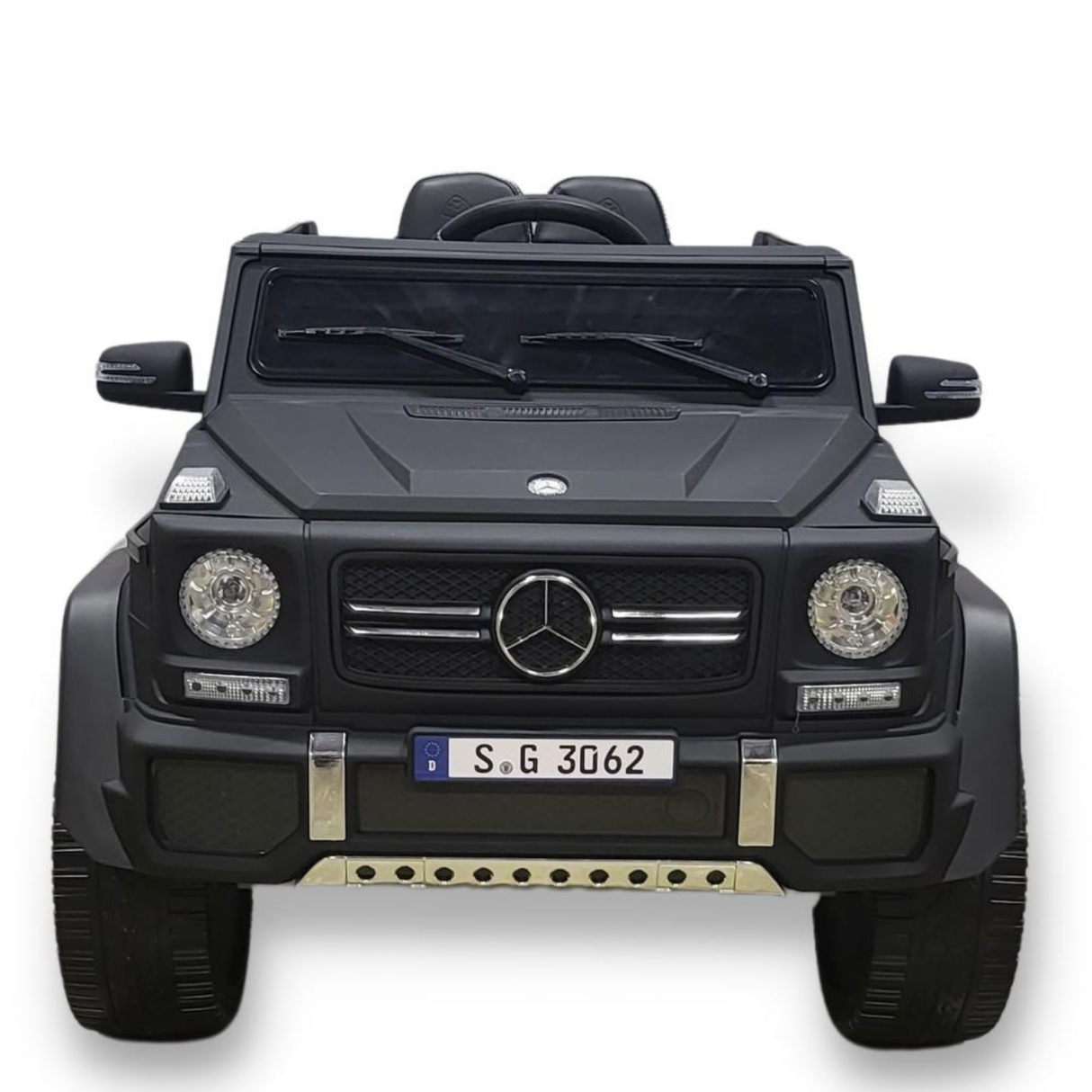 A matte black toy car, the 12V Mercedes-Benz Maybach G650s kids ride-on, is shown from the front. It features detailed headlights, a logoed grille, and a visible steering wheel for childrens use. It displays the license plate S G 3062.