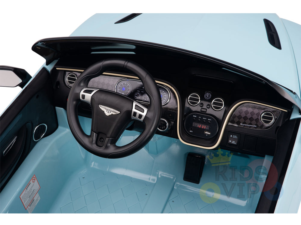 Interior of the Blue 12V Bentley GTC Kids Licensed Ride On Car features a black steering wheel, various dashboard gauges and controls set against a brown and black pattern. It offers a plush leather seat for comfort.