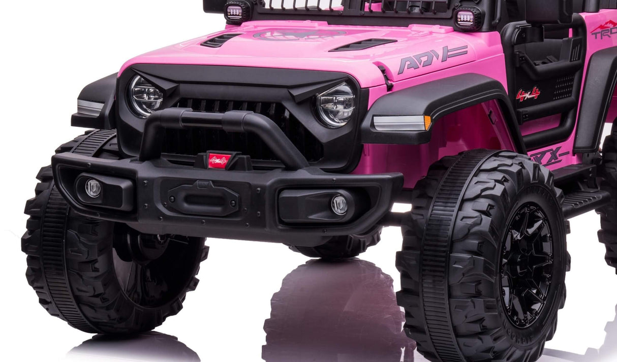 The pink 24V/2WD Xtreme Edition Ride on Truck boasts rugged off-road styling with Eva Wheels, formidable black tires, a detailed front grille, headlights, and a small bumper. This 2-seater marvel stands proudly on a reflective white surface.