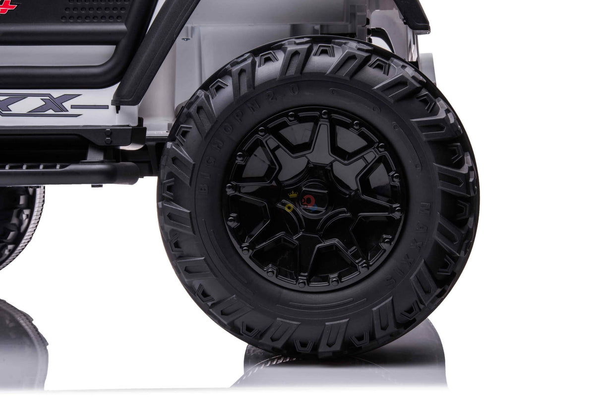 Close-up of a large, rugged black tire with deep treads and an eye-catching wheel design. Labeled BIG JOHN 24X9-12, its mounted on a White 24V/4WD Xtreme Ride on Truck, featuring Eva Wheels and Leather Seats, exuding a robust presence against the neutral background.
