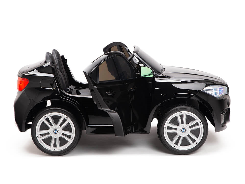 The Black 12V Licensed XXL BMW X6 Ride-On Car features a sporty, 2-seater design with an open roof, silver rims, visible headlights, and an open driverโs door. Styled for fun, this sleek black car stands out against the white background.