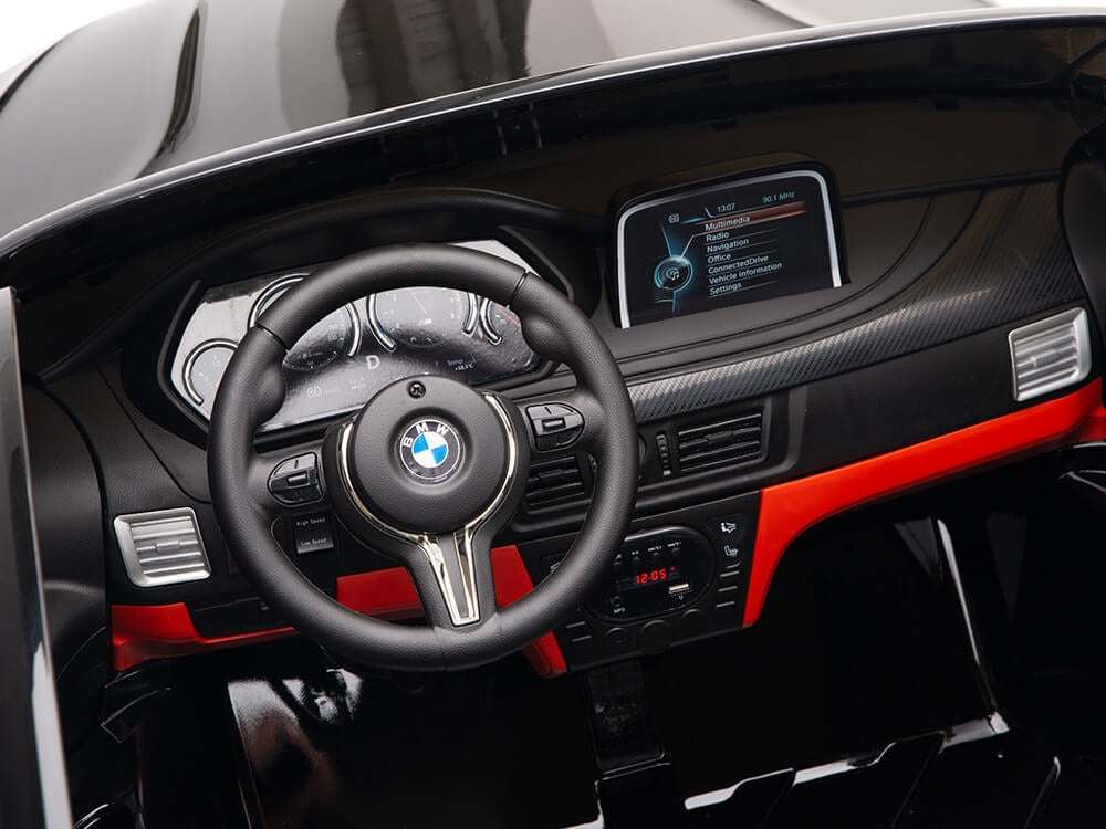 The Black 12V Licensed XXL BMW X6 Ride On Car boasts a sleek, modern interior with a steering wheel, red-accented dashboard, and digital display. This remote-control car delivers an authentic driving experience for kids with multiple dials.