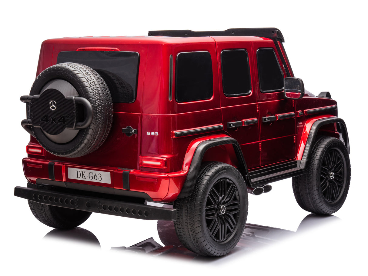 A rear and side view of a Red Metallic 2x24V/4WD Platinum XXL Mercedes G63 Ride-On Truck shows a spare tire, tinted windows, DK-G63 license plate, remote control access, on a reflective white surface.