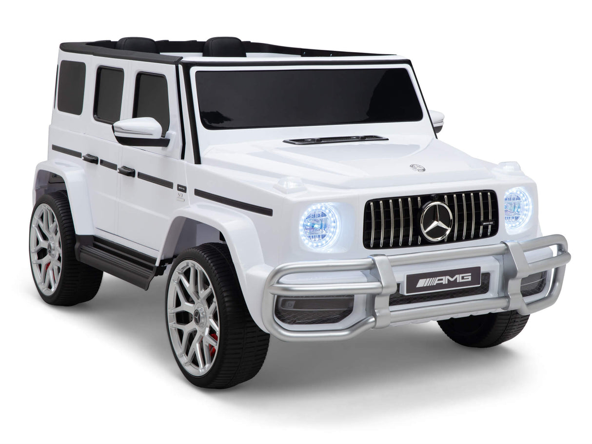 This white ride-on car, the 2 Seats 4x4 Official Mercedes Benz G63 Complete Edition, mimics a luxurious Mercedes-Benz with detailed styling. It showcases realistic wheels, iconic logos on the grille, chrome accents, visible headlights, and a black interior for an authentic flair.