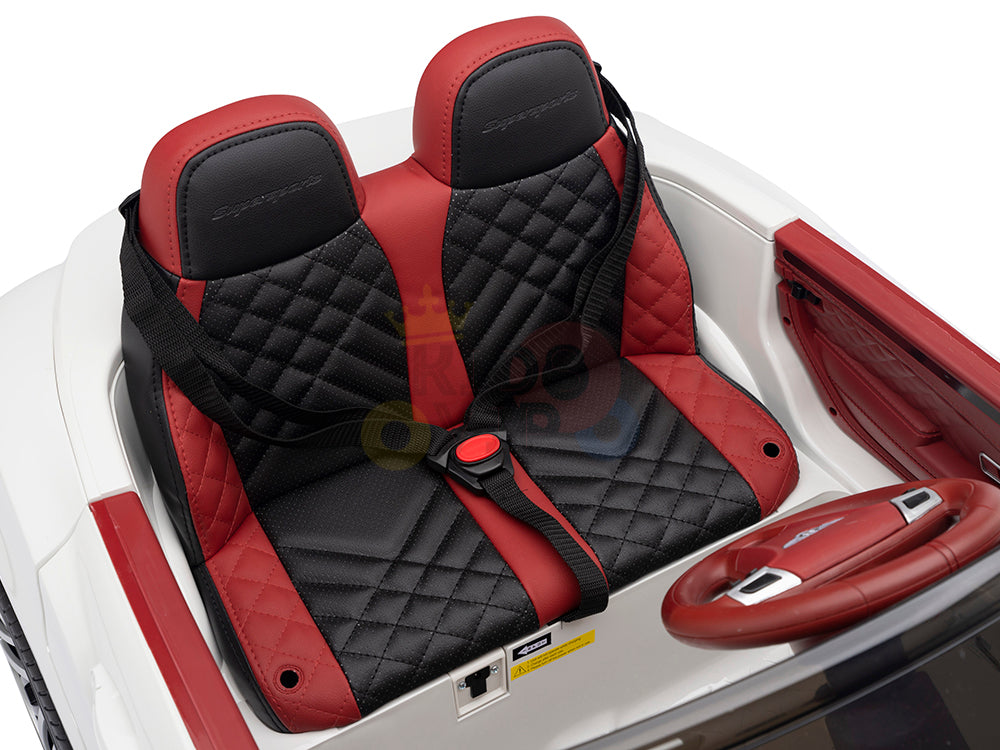 Close-up of the White 12V Bentley GTC Kids Licensed Ride On Cars interior, showcasing two black and red quilted leather seats with seatbelts, a matching steering wheel, and dashboard controls. This miniature version mirrors the craftsmanship of a real Bentley.