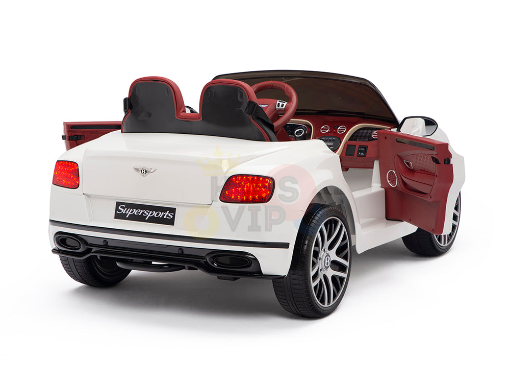 The White 12V Bentley GTC Kids Licensed Ride On Car offers a genuine driving experience with sporty rubber wheels, leather seats, an open drivers side door, and a detailed dashboard. The vehicle, branded Supersports, includes a remote control and features a classic white and red design.
