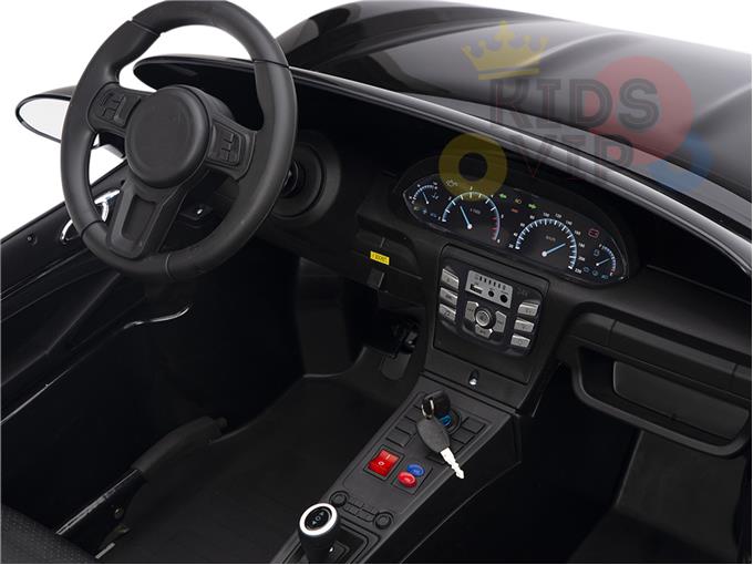 The interior of the Black 24V XXL SuperSport Big Kids Ride On Car features ECO leather seats, a black steering wheel, a dashboard with speedometers, control buttons, and an ignition key fob. The brand logo is slightly visible on the top right corner.