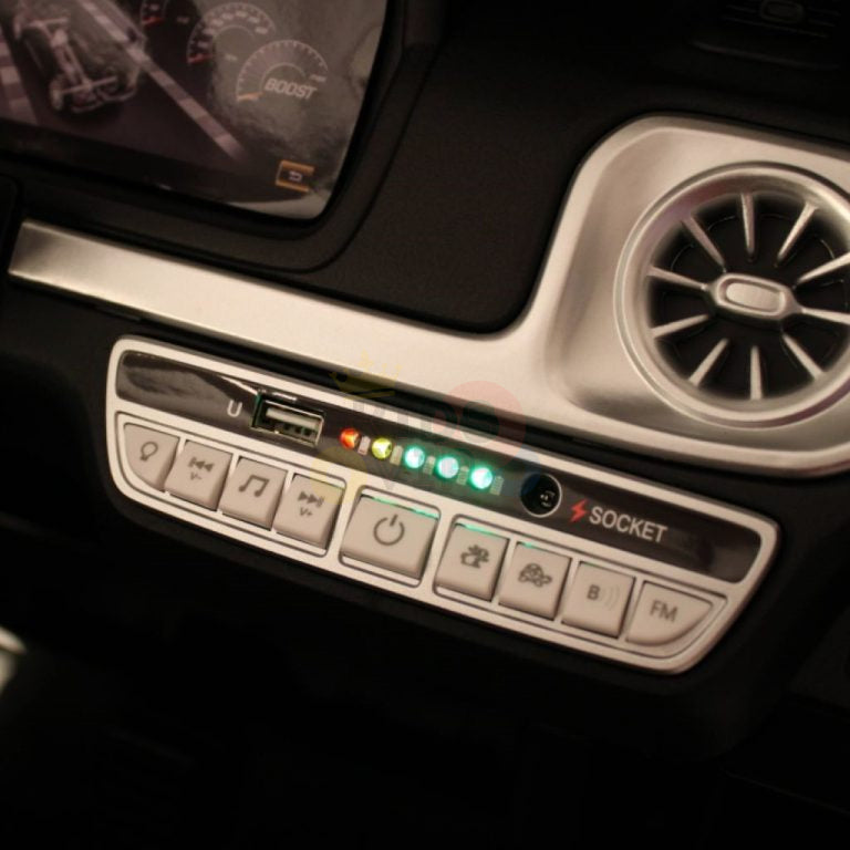 Close-up of the dashboard of a Black 24V 2 Seats 4x4 Official Mercedes Benz G63 Kids Ride On Car with RC. Various buttons and controls are visible, alongside illuminated LED lights labeled USB and socket. Partially seen air vent and digital display enhance the luxurious ride powered by a 24V battery system.