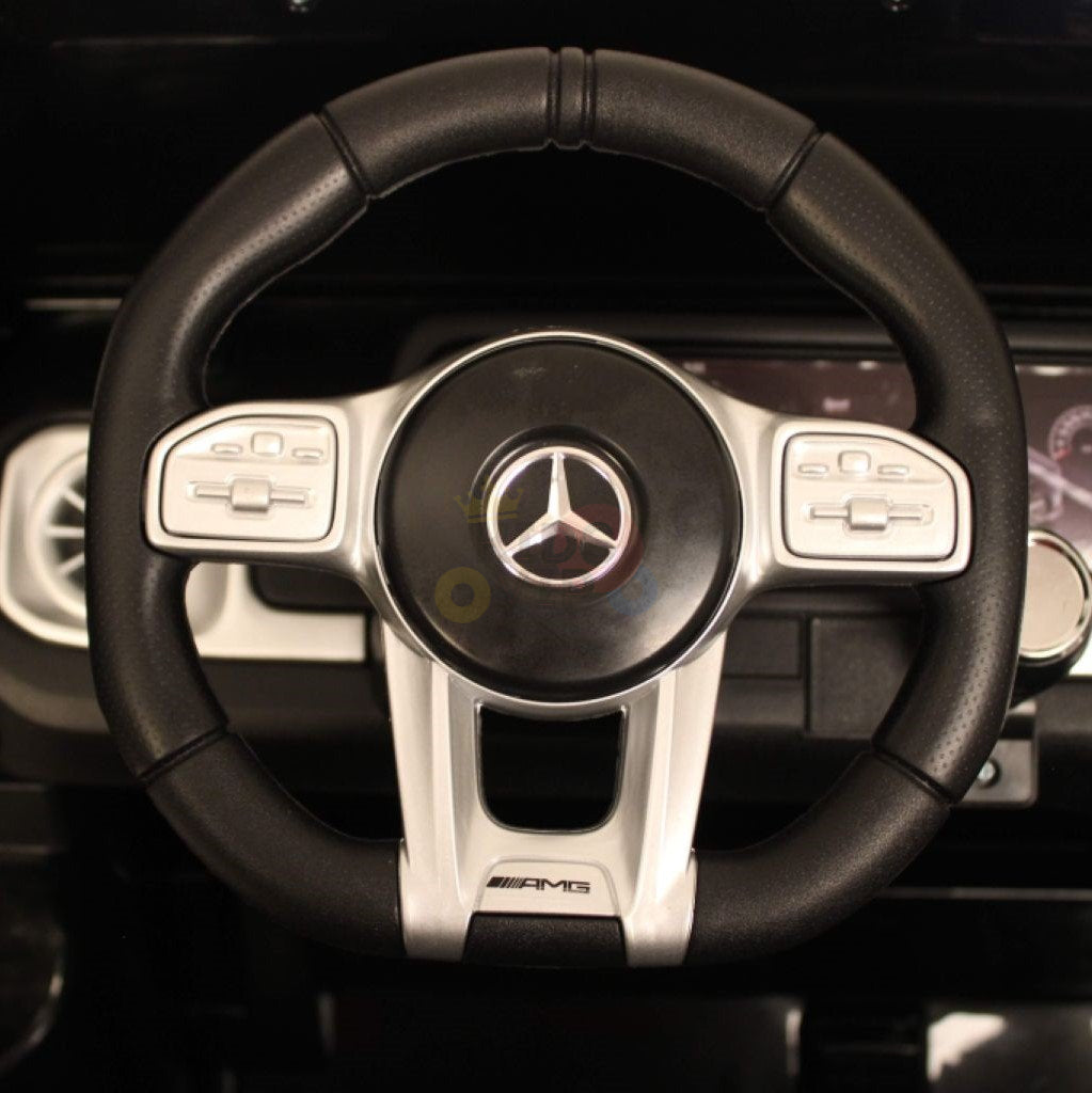 A close-up of the black and silver steering wheel, adorned with the Mercedes-Benz logo at its center, mirrors that of a G63. Equipped with control buttons and set against a backdrop of dashboard instruments, it perfectly suits the Black 24V/4x4 Official Mercedes Benz G63 Ride On Car with RC for kids.