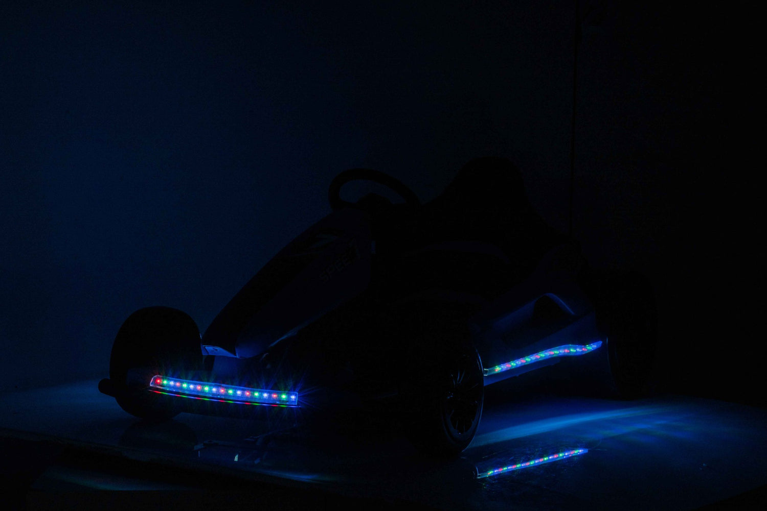 A silhouetted Pink 24V Ultra-Violent Big Kids Complete Edition Drifting Go-Kart with LED lights illuminates wheels and frame in a dim setting, perfect for high-speed drifting adventures.