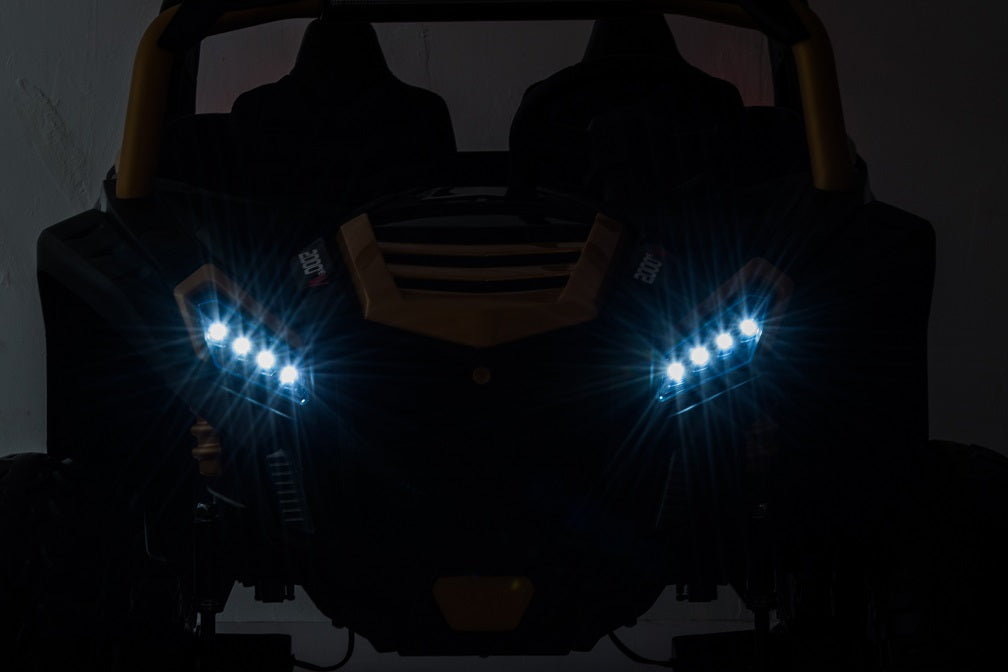 A dark image features a vehicle with illuminated LED headlights, forming a distinctive pattern that partially reveals the Black 24V/180W XXL Big Kids Blade XR Ride on Buggy, hinting at its ECO leather seats and inflatable rubber tires against the shadowy background.