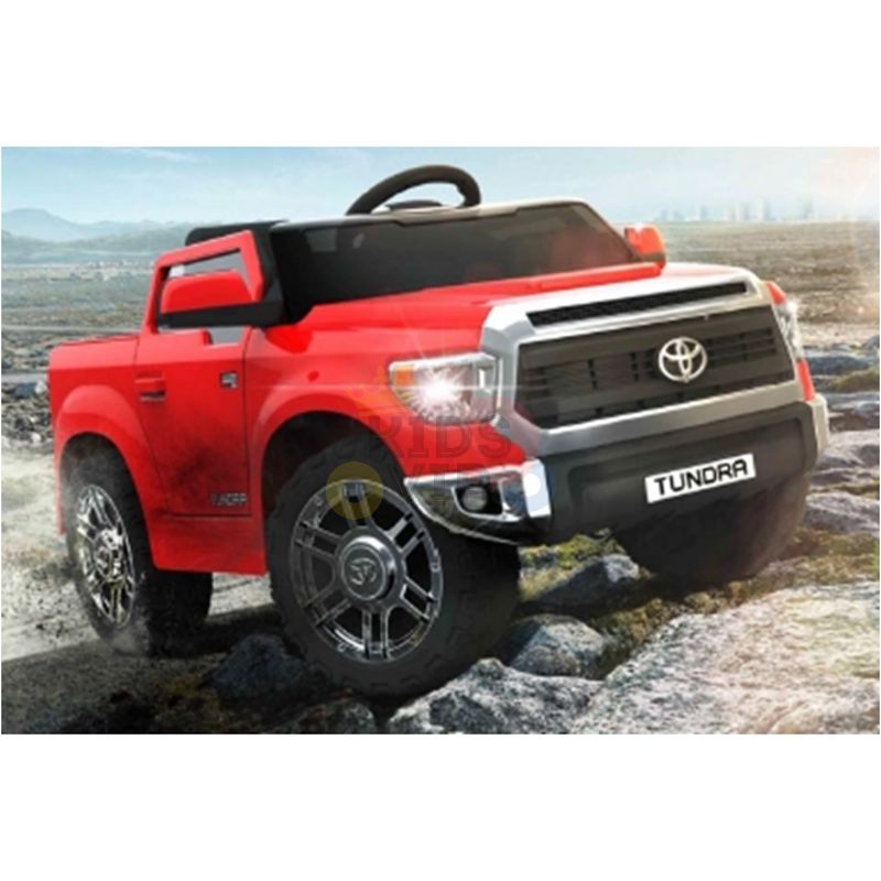 A Red 12V Licensed Upgraded Toyota Tundra 1 Seater Kids Ride On Truck with RC sits on rocky terrain. The Tundra plate is visible as the charming toy faces slightly left, featuring shiny wheels and parental remote control operation.