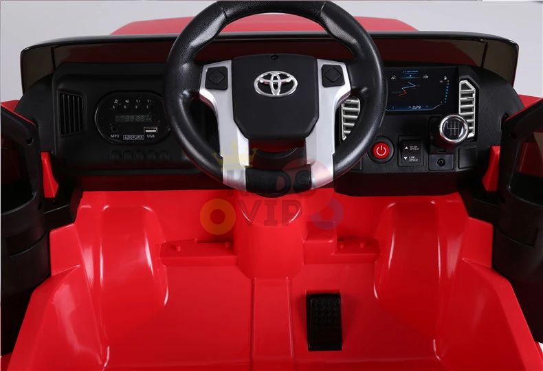 The Red 12V Licensed Upgraded Toyota Tundra Kids Ride On Truck includes a black and silver steering wheel with a Toyota logo, various buttons, speedometer, small screen, and a vibrant red interior for imaginative adventures.