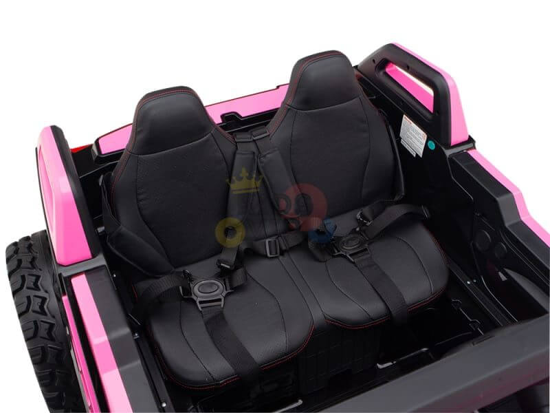 The image shows the interior of a Pink 24V/4X4 Dune Buggy Ride On UTV. This kids XXL edition includes two black seats with red stitching, secure seat belts, rubber wheels for durability, and a spare tire mounted at the back.