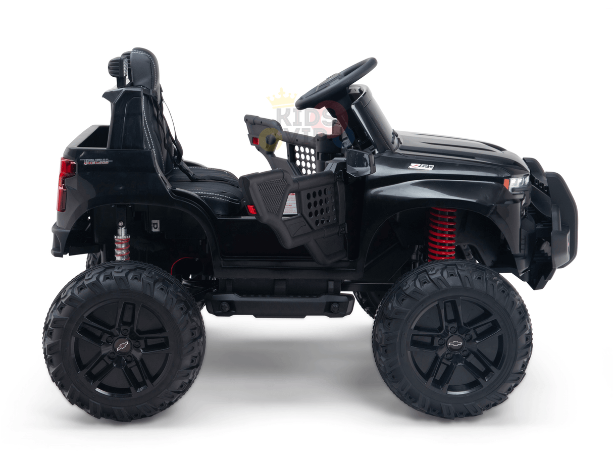 Side view of the Black Official 24V Chevrolet Silverado Lifted Kids Ride-on Truck, resembling an off-road vehicle with large wheels, red suspension springs, steering wheel, and a seatbelt-equipped seat. Powered by a 24V battery for endless adventures.