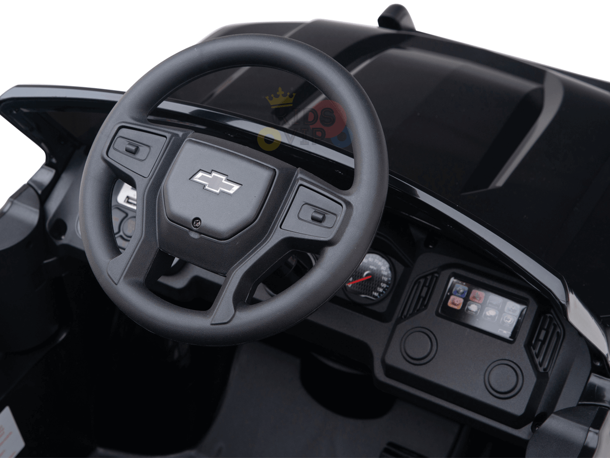 Interior view of a Black Official 24V Chevrolet Silverado Lifted Kids Ride-on Truck, featuring the steering wheel with iconic logo, dashboard controls, speedometer, and infotainment display—an ideal sleek black design for young drivers.