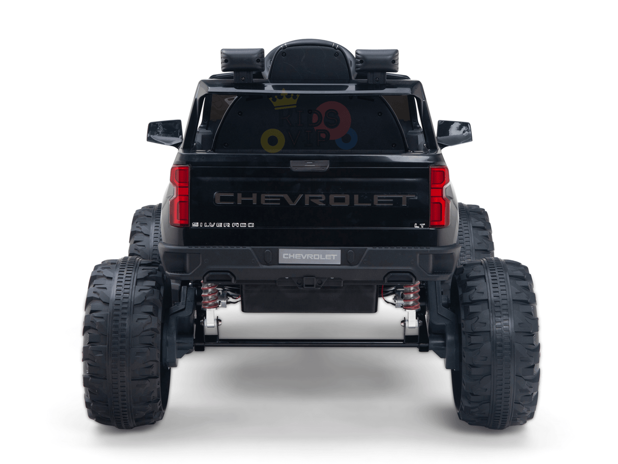 Rear view of a Black Official 24V Chevrolet Silverado Lifted Kids Ride-on Truck with oversized tires and Chevrolet branding on the tailgate. The rear window features colorful stickers like a crown and geometric shapes, offering endless adventures.