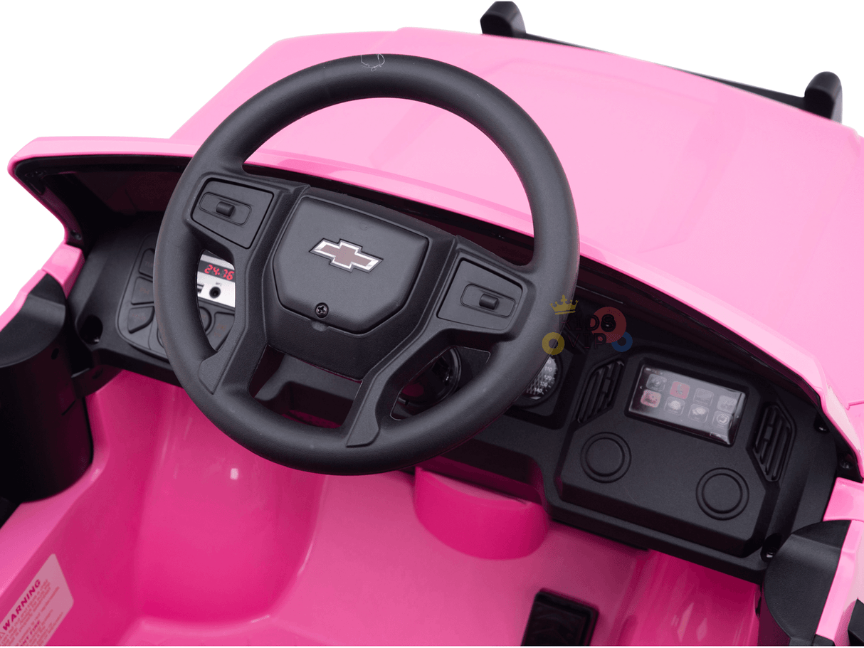 Interior view of a pink 24V Chevrolet Silverado kids ride-on lifted truck with black steering wheel and Chevrolet logo, featuring simple dashboard controls.