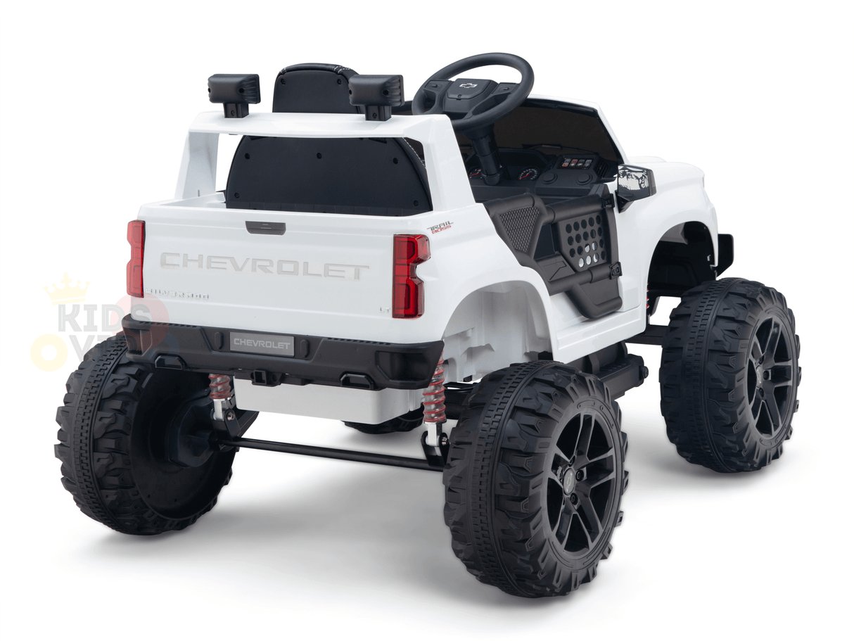 The White 24V Chevrolet Silverado Kids Licensed 1 Seater Ride On Lifted Truck features oversized black wheels, a realistic steering wheel and dashboard, Chevrolet branding on the back, and a robust suspension system for adventurous play.