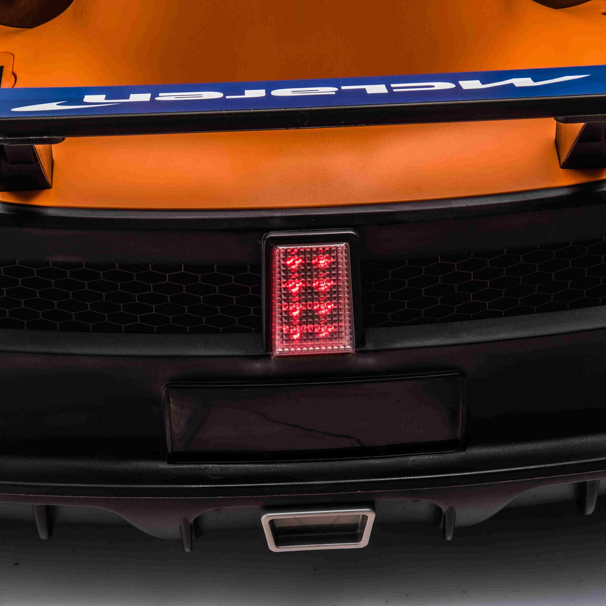 A close-up of a cars rear with the McLaren logo on a blue spoiler evokes the Orange 24V Official Complete Edition McLaren Super Drifting Go-Kart. The vibrant orange body contrasts with the red light and black honeycomb grill, while a unique exhaust shape completes this sleek design.