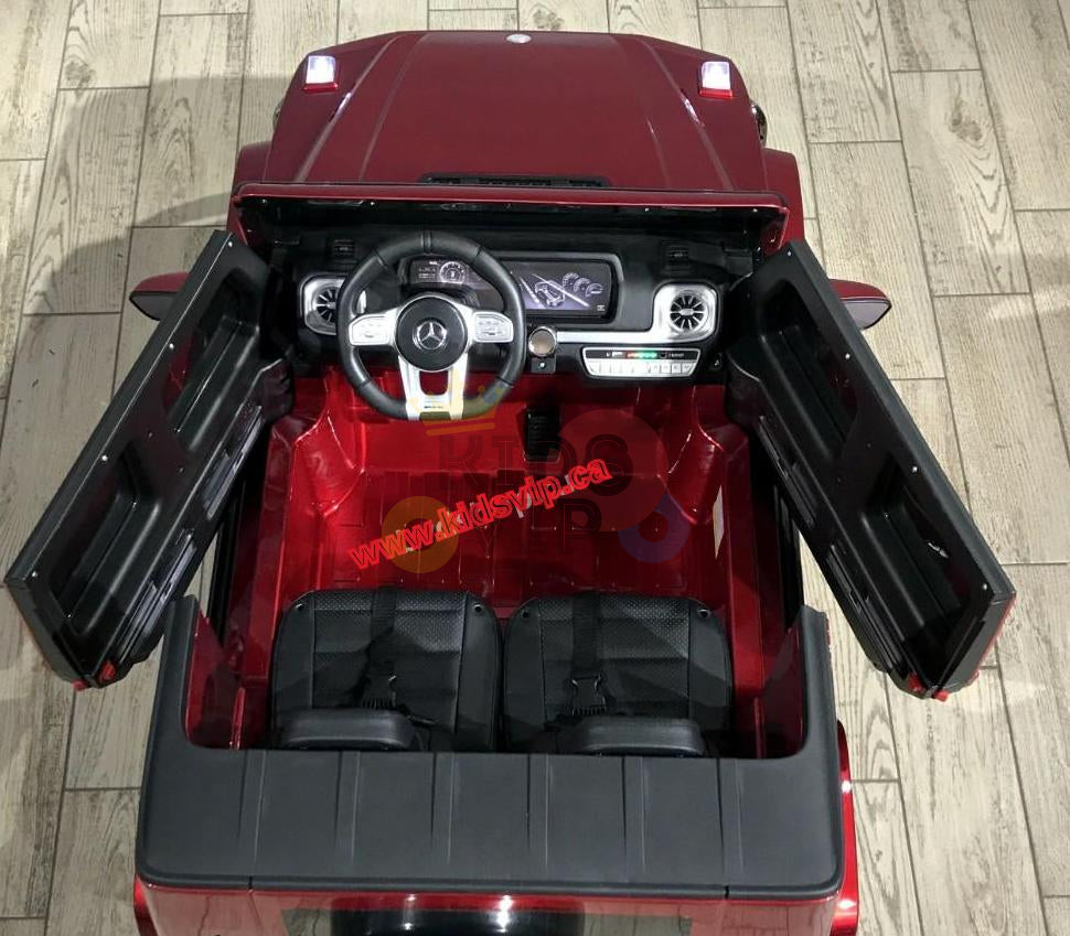 A birds-eye view shows the red 2 Seats 4x4 Official Mercedes Benz G63 Complete Edition, a kids ride-on car with open doors. It features a detailed dashboard, two black seats, powered by a robust 24V battery, and has a wooden floor.