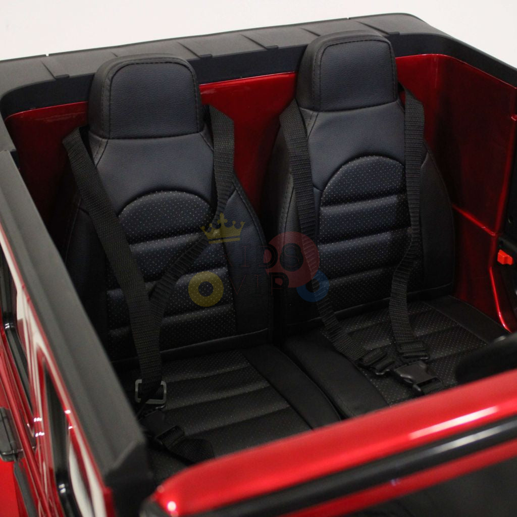 The image features the interior of a 2 Seats 4x4 Official Mercedes Benz G63 Complete Edition Red 24V Kids Ride On Car, highlighting its two black leather-like seats with safety harnesses. Its vibrant red exterior and detailed stitching add realism, powered by a 24V battery for thrilling rides.