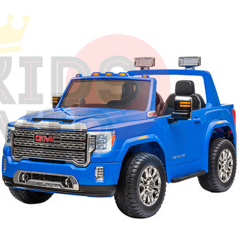 A blue 2-seater GMC Sierra 4WD kids ride-on car with chrome detailing, lights, detailed grille, large wheels, leather seats, and RC. The white background features a partial logo.