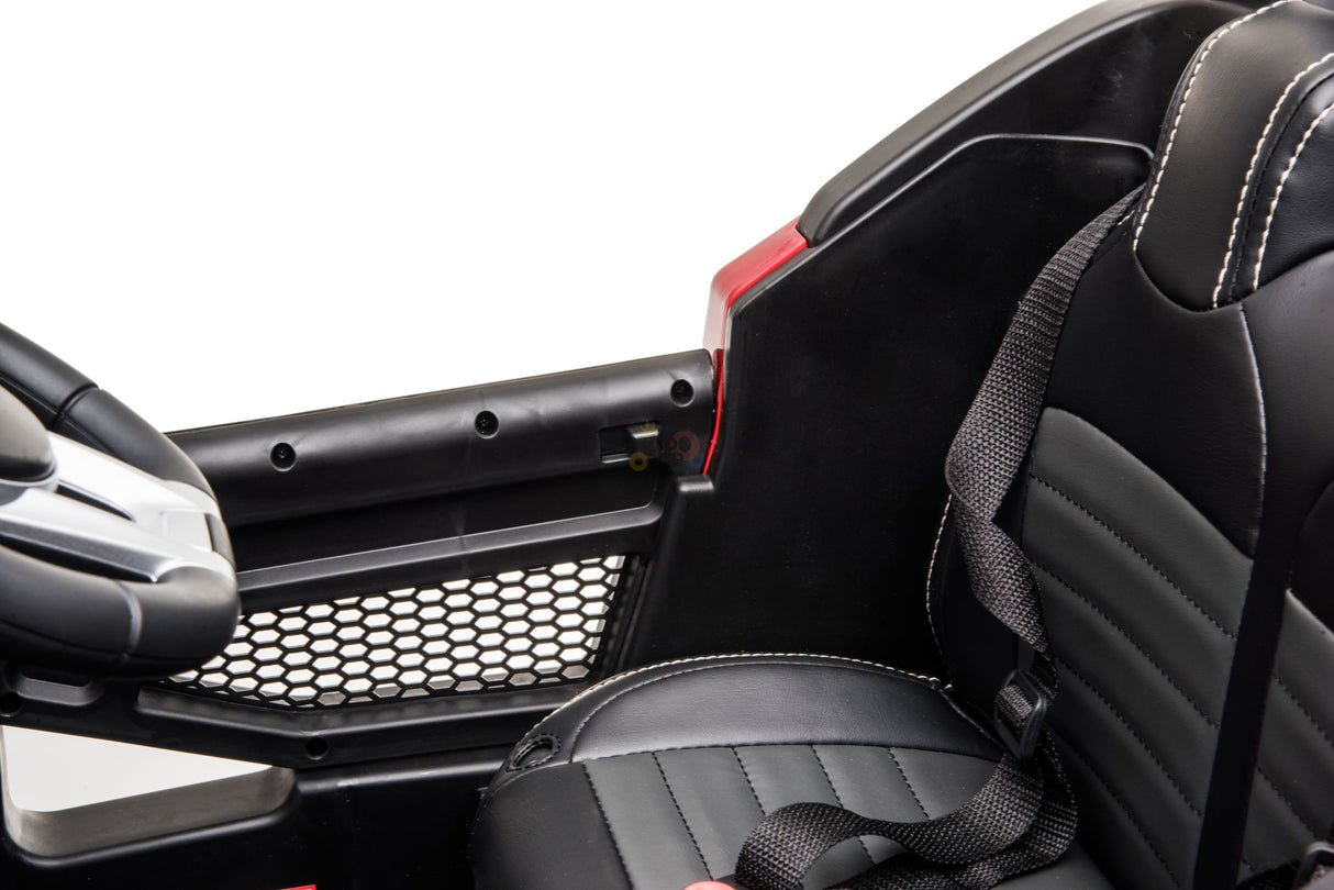 Close-up of a black and red interior from the Official 12V Mercedes Unimog Junior 4X4 Kids Ride On UTV, showcasing a steering wheel, mesh side detail, and a black seat with white stitching and seatbelt against a plain white background.