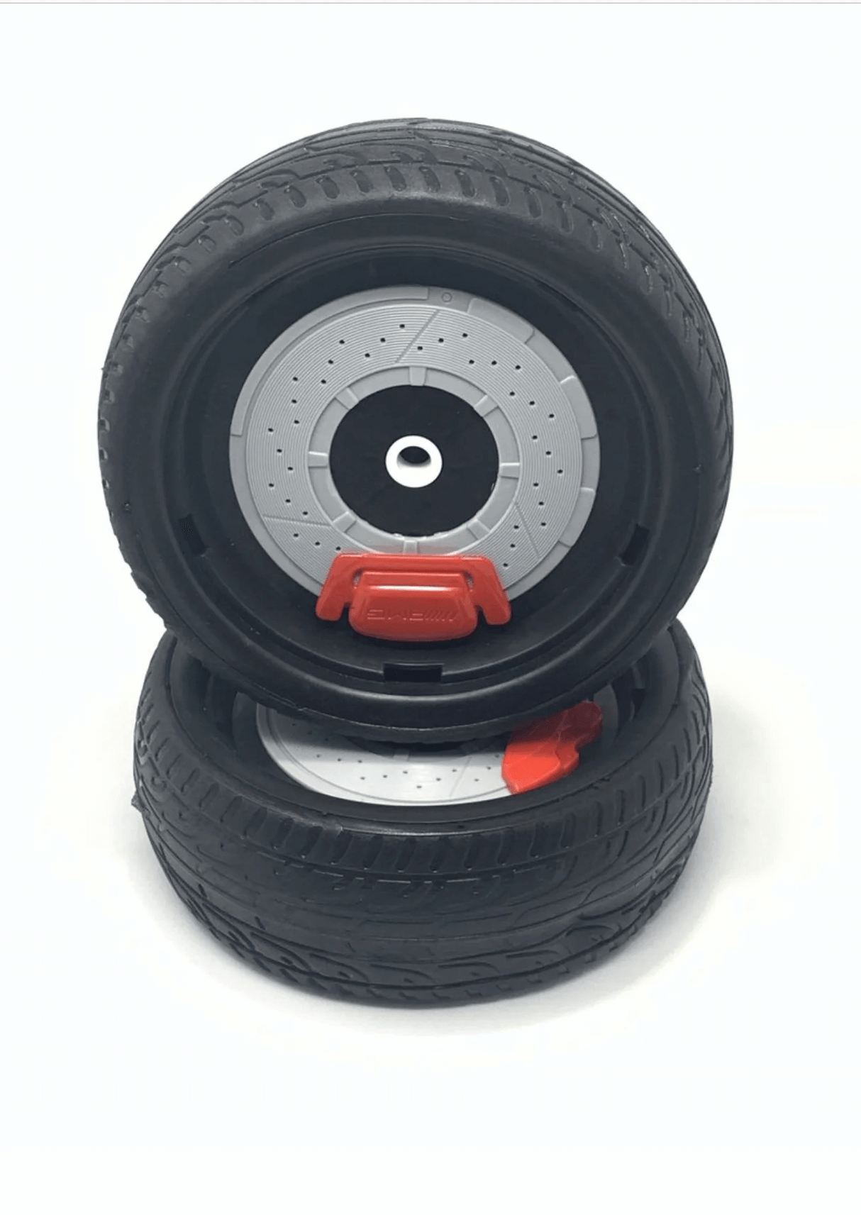 Two black toy car tires featuring treads are stacked vertically. The top tire, resembling those on a 12v Bugatti Chiron ride-on car, has a detailed gray and silver rim with a red accent and stands upright on another lying flat.