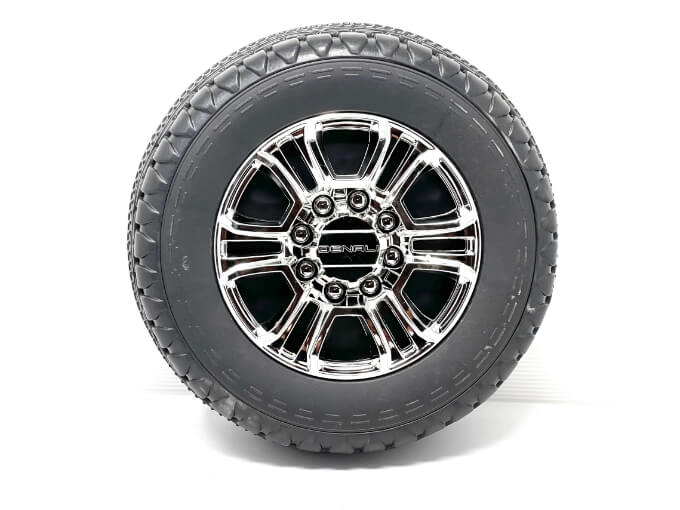 The Enhance Your Ride with 12v/2 Seater GMC Sierra Rear Eva Rubber Wheel features a black tire with a shiny chrome rim, multiple spokes, and a logo-branded center hub. The tread pattern evidences enhanced traction, all set against a white background.