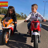 Two children joyfully ride their INJUSA 12V Honda bikes under a sunny sky. The girl zips along on an orange motorcycle, while the boy cruises beside her on the Red INJUSA 12V Honda Naked Edition. Palm trees and a clear sky frame the scene, with a Made in Spain label at the top left.