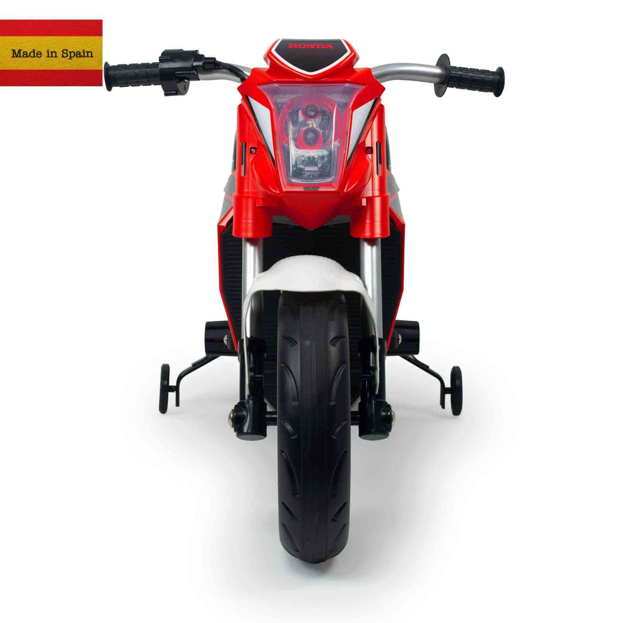 The front view of the Red INJUSA 12V Honda Naked Edition Ride On Bike for Kids shows a childs toy motorcycle with training wheels, a central headlight, and the Honda logo. A Made in Spain text paired with a small Spanish flag is seen in the top left corner for authenticity.