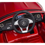 Close-up of a Red 12V Mercedes Benz Maybach S650 Kids Ride On Car dashboard, featuring the Mercedes-Benz emblem on the steering wheel. Displays and controls gleam against a shiny red background, capturing the essence of the luxury interior.