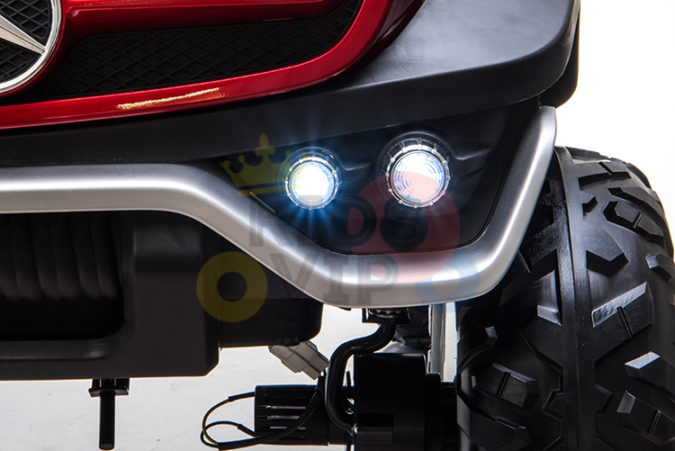 Close-up of the Blue Official 12V Mercedes Unimog Junior 4X4 Kids Ride On UTVs front end, showcasing LED headlights, a silver bumper, and visible tire tread. The right headlight is lit, and parts of the suspension are exposed—ideal for adventurous kids rides.