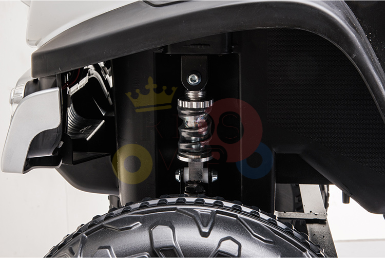 Close-up of the suspension on a Blue Official 12V Mercedes Unimog Junior 4X4 Kids Ride On UTV, showing detailed coil spring and tire tread within a dark framework with bumper visible on the left.