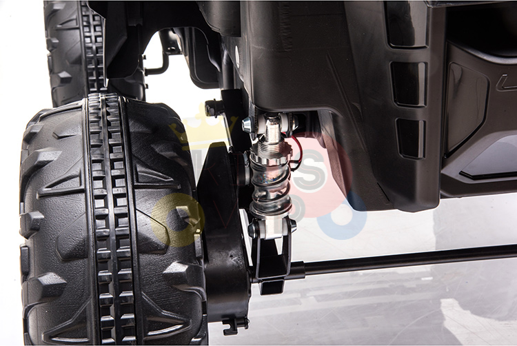 A close-up of the Blue Official 12V Mercedes Unimog Junior 4X4s suspension shows its large knobby tire, coiled spring shock absorber, and part of the chassis. The blurred background hints at the terrains this kids ride-on UTV conquers easily.