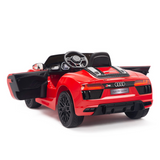 The Red 12V Audi R8 Licensed 1-Seater Ride On Car, a replica of the Audi R8 Spyder, sports an open drivers side door, detailed rear lights, and black interior. From a rear side angle, it showcases the Audi logo on the steering wheel and upgraded EVA rubber wheels for enhanced realism.