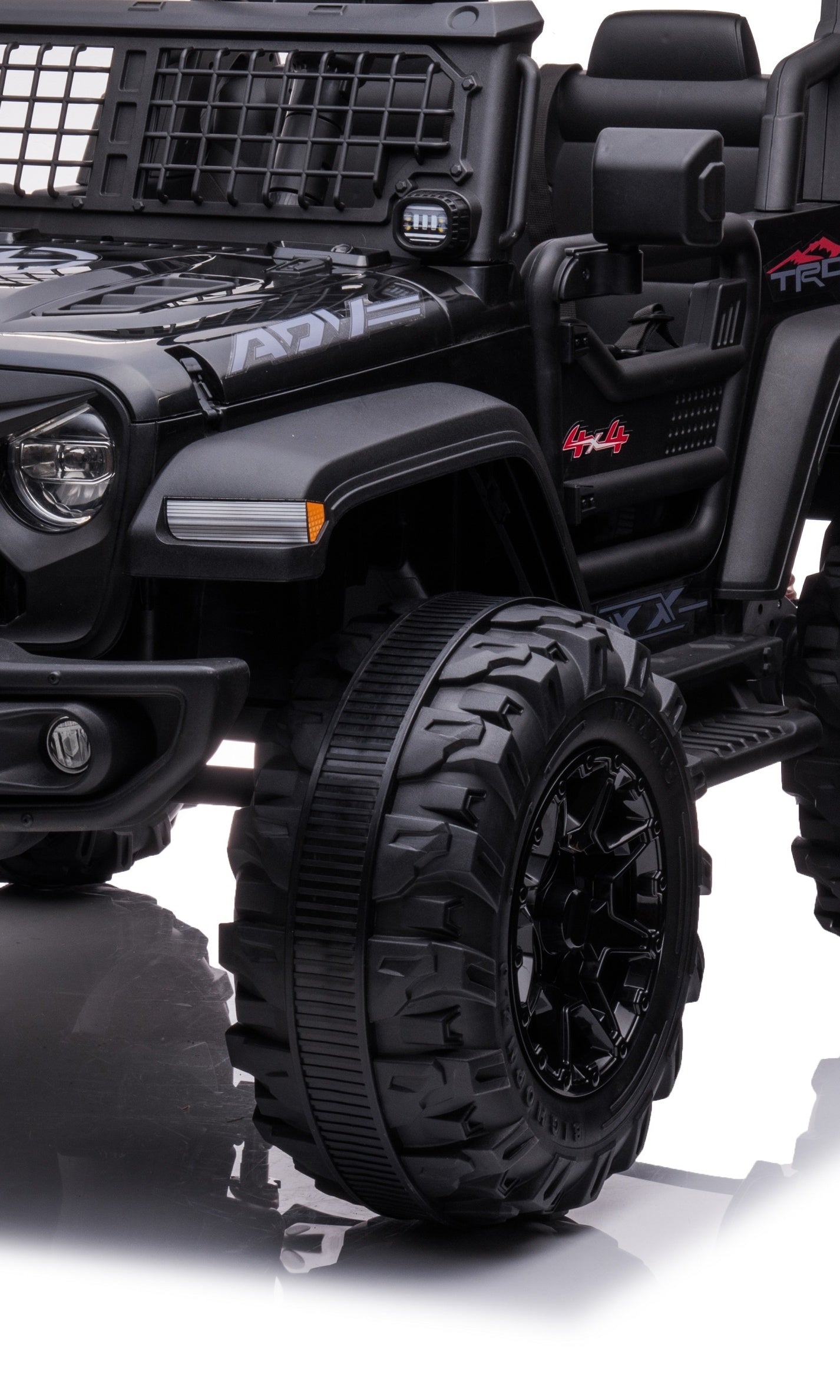 A close-up of the Black 24V/2WD Xtreme Edition Ride-on Truck flaunting rugged Eva wheels and intricate details. With leather seats, a grid-like hood pattern, and branding accents, its side mirror and part of the interior appear against a white background.
