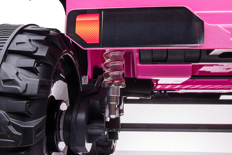 Close-up of the rear wheel and suspension system of the Pink 24V/2WD Xtreme Edition Ride on Truck, featuring a large black EVA wheel with rugged tread, a red reflector above it, and metal suspension parts beneath the bright pink 2-seater body.