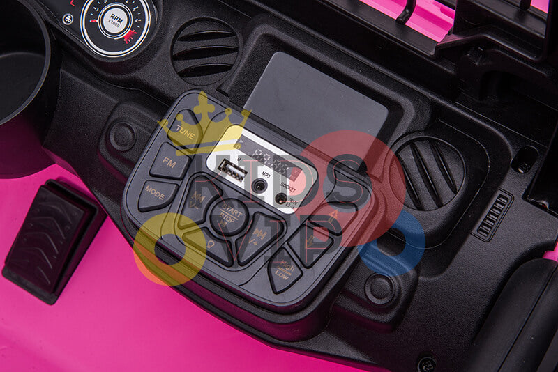 Close-up of the Pink 24V/4WD Xtreme Ride on Trucks toy dashboard with a control panel labeled for tune, FM, mode, stop, start, and volume. This kids electric truck features a USB port and auxiliary input, all set against a pink background.
