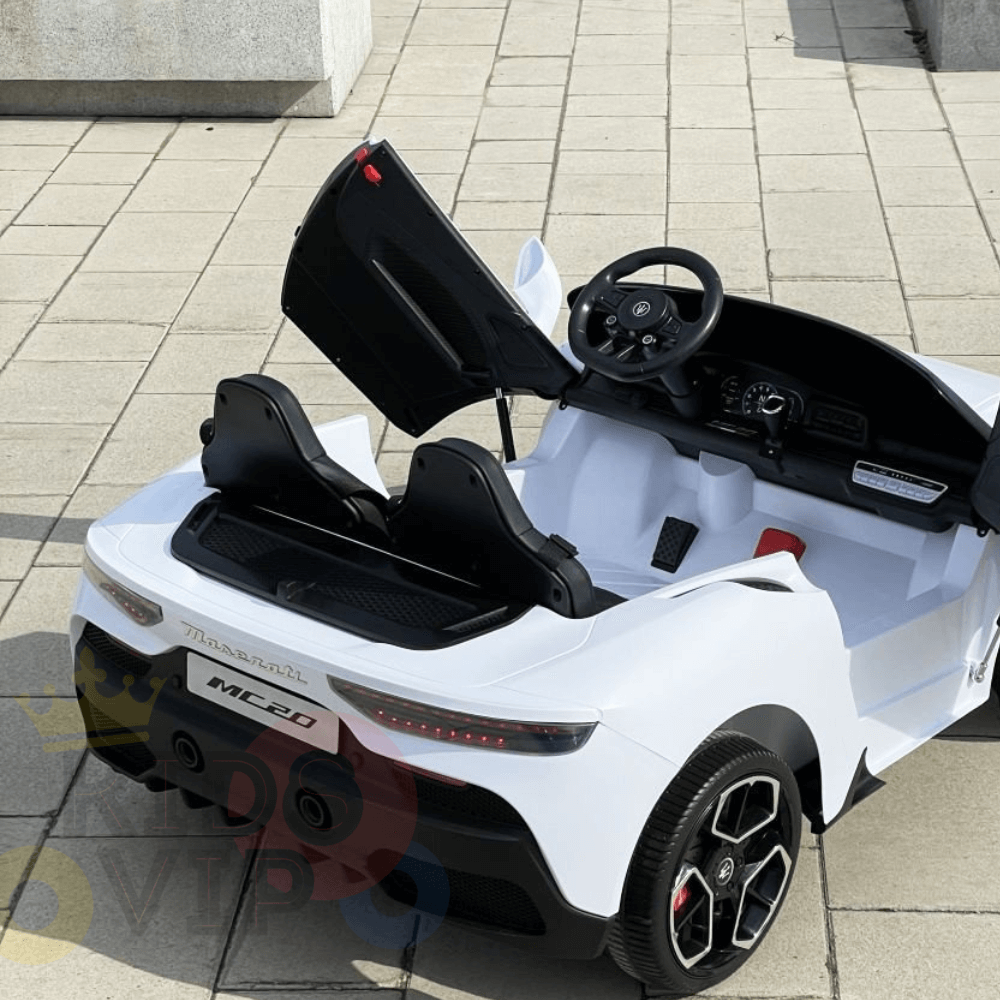 A white XXL Maserati MC20 ride-on sports car featuring open scissor doors, detailed dashboard, two leather seats, and rear branding is parked on a tiled outdoor surface.