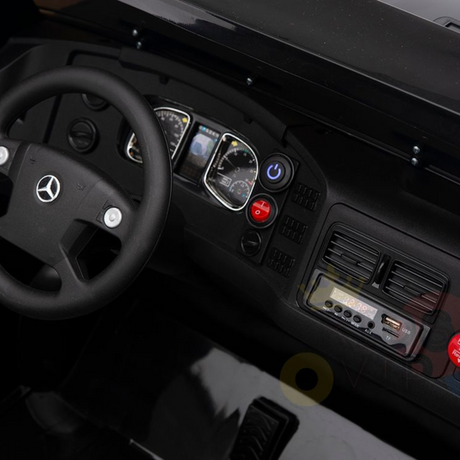 Close-up of a sleek car dashboard with a Mercedes logo on the steering wheel, akin to the Black 24V XXL Mercedes Benz Zetros Kids Ride On Truck. It features a speedometer, control buttons including a red one, air vents, and a digital display with USB ports, mirroring its modern design.