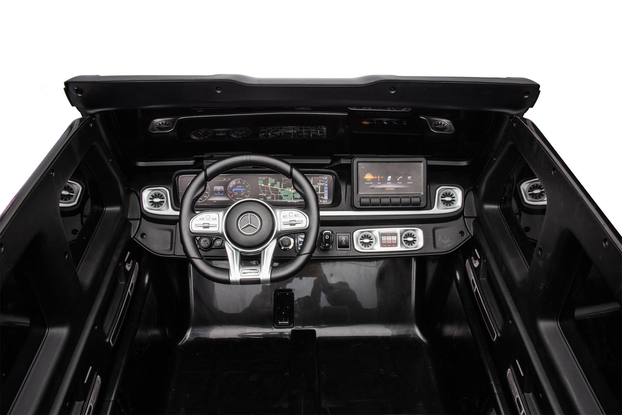 The Black Mercedes G63 XXL 24V Kids Ride-On Truck – Platinum Edition features a luxury interior with a logo on the steering wheel, digital instrument panel, and touchscreen controls. This model includes MP4, dual batteries, 4WD, EVA tires, leather seats, and sleek modern dashboard designs.