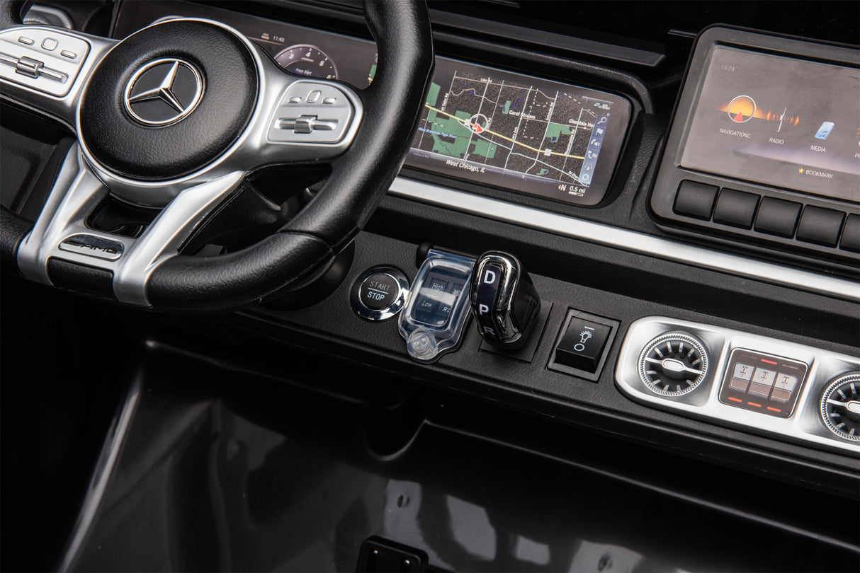 A close-up of a car dashboard featuring a Mercedes-Benz steering wheel evokes the Black Mercedes G63 XXL 24V Kids Ride-On Truck – Platinum Edition, with touchscreen navigation, control screens, gear shift lever, and buttons resembling its 4WD EVA tires and leather seats experience.