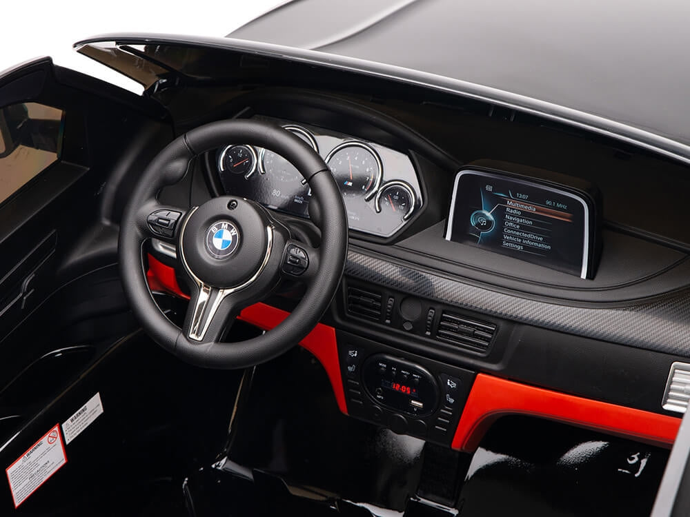 The Black 12V Licensed XXL BMW X6 Ride On Car features a steering wheel adorned with the iconic BMW logo, analog dashboard gauges, and a central digital display. Red trim accents various controls, embodying luxury in this 2-seater ride-on car, complete with remote control.