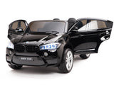 The Black 12V Licensed XXL BMW X6 Ride On Car with remote control features open doors, illuminated headlights, and a glossy finish. Positioned against a white background, this stunning model is ideal for kids, capturing the elegance of the BMW X6M.