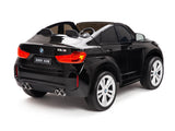 The Black 12V Licensed XXL BMW X6 Ride On Car With Remote Control is a sleek toy resembling the BMW X6M, featuring a detailed design with large white wheels, rear lights, dual exhaust pipes, and a small steering wheel. This 2-seater ride is angled to highlight its craftsmanship.