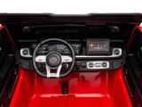 Interior of the Red 2x24V/4WD Platinum XXL Mercedes G63 Ride-On Truck highlights its black-and-silver steering wheel, digital display, glossy red flooring, metallic air vents, and control buttons. Features include MP4 player, EVA wheels, leather seats, and remote control for easy use.