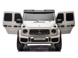 The White 2x24V/4WD Platinum XXL Mercedes G63 Ride-On Truck offers open doors, a black roof, tinted windows, and a DK-G63 plate. It features an iconic grille emblem and remote control access against a white background. Enjoy MP4 entertainment with EVA wheels and leather seats in this luxury SUV replica.