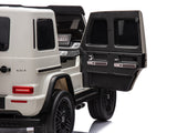 The White 2x24V/4WD Platinum XXL Mercedes G63 Ride-On Truck features a sleek black interior and dashboard, black wheels and taillights, all set against a white backdrop. This luxury SUV for kids offers MP4 controls, EVA wheels, leather seats, and remote access. Rear door open for added style.